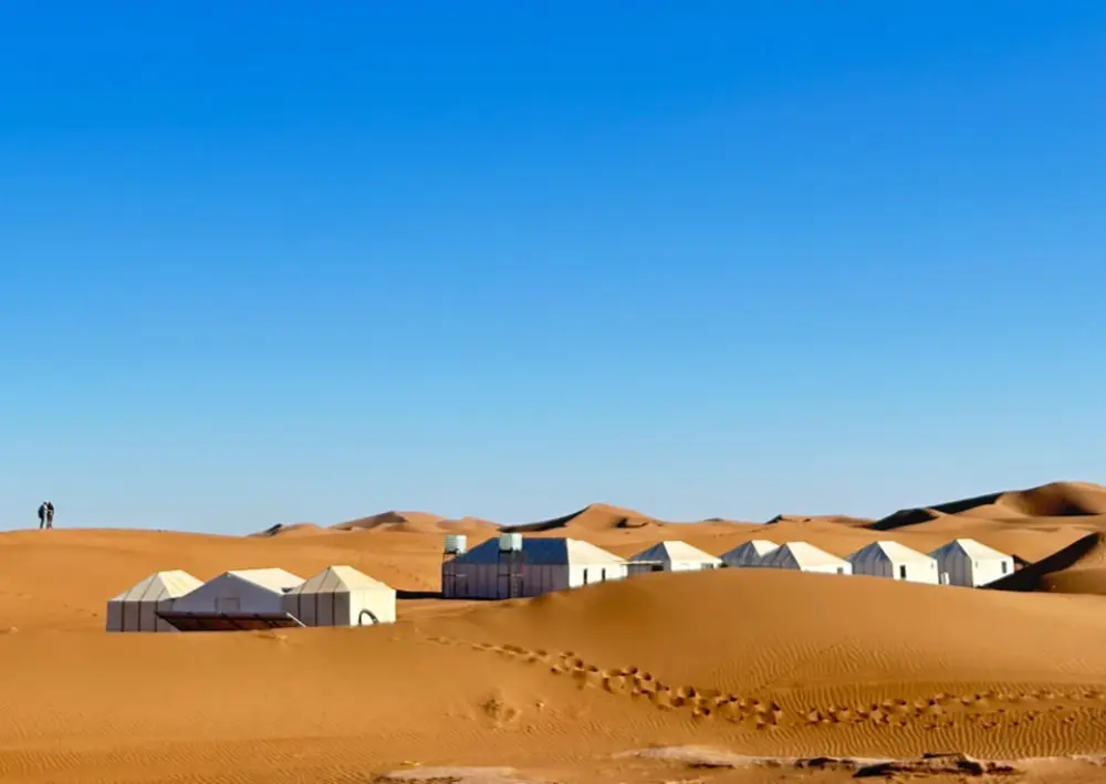 Tentes blanches d’un camp de désert au milieu des dunes sous un ciel bleu