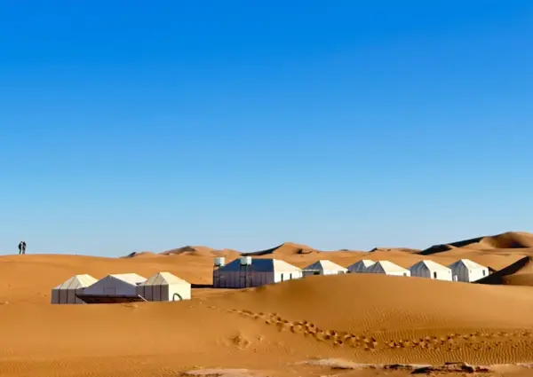 Tentes blanches d’un camp de désert au milieu des dunes sous un ciel bleu